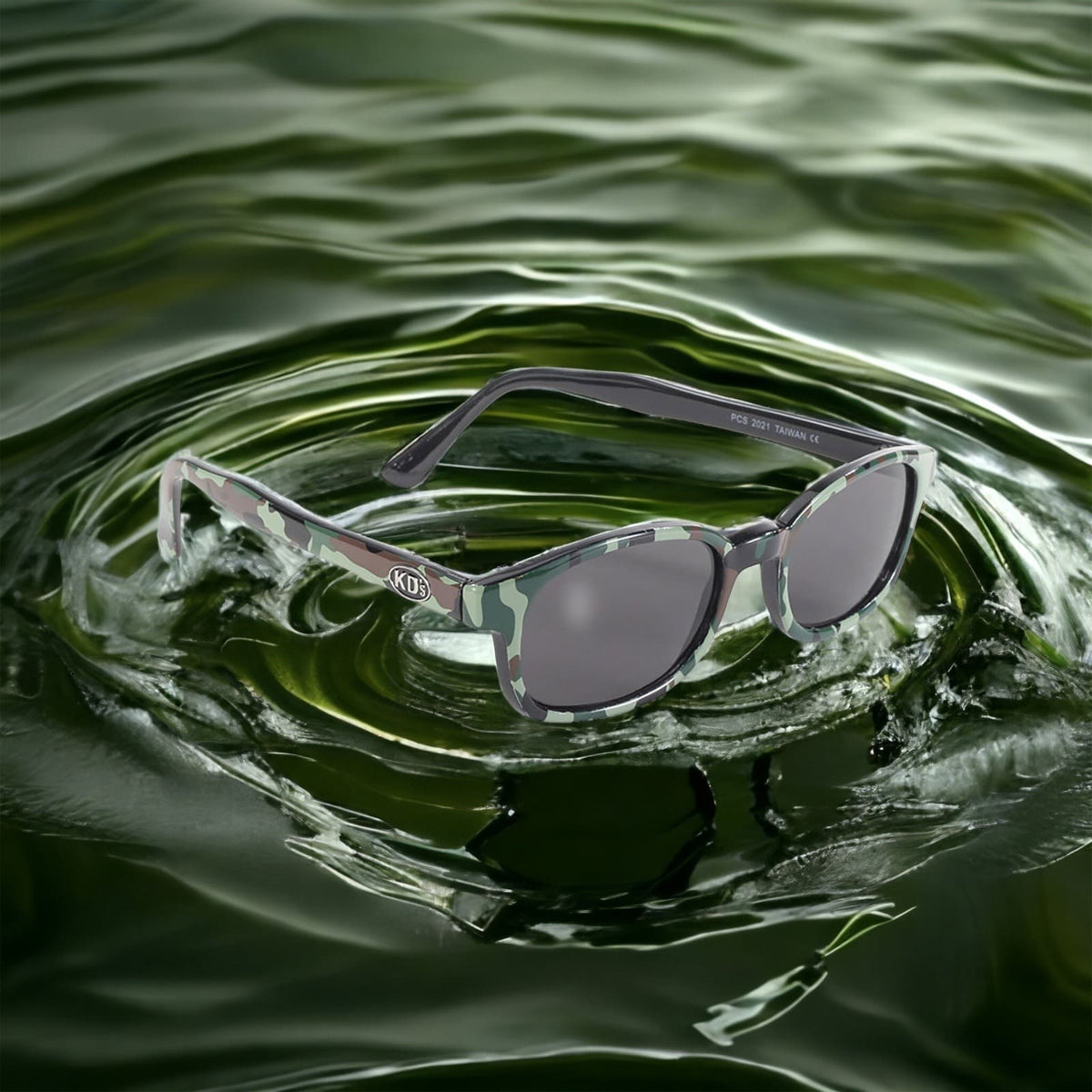 The sunglasses KD's 2021 ideal for sportsmen with grey lenses and a frame with military motifs placed on the water.