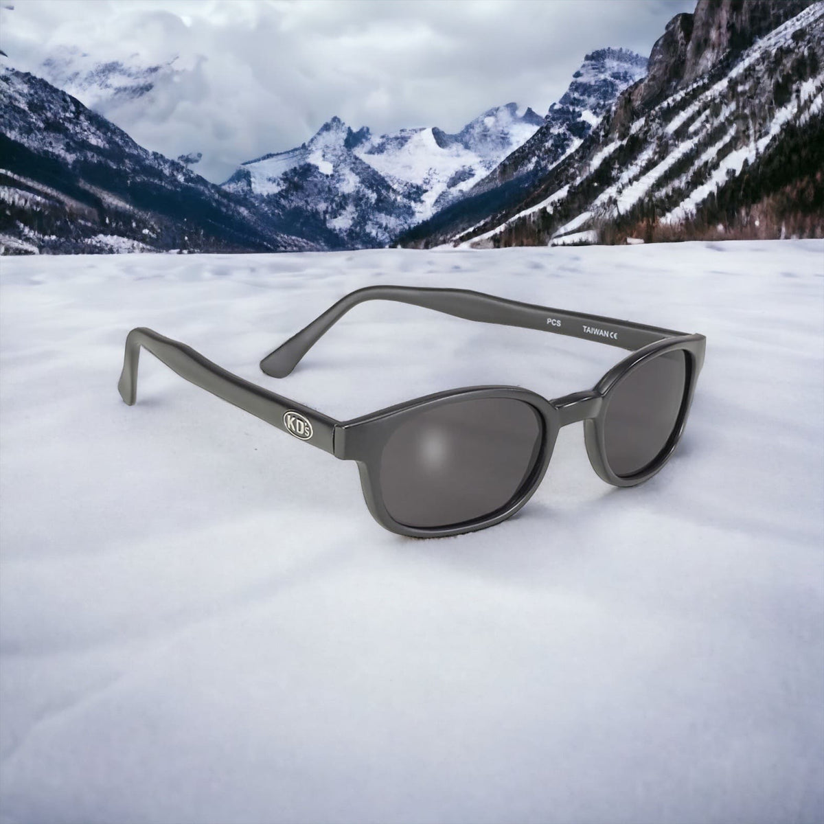 KD's 21120 sunglasses that fit under a motorcycle or ski helmet. Worn by SAMCRO bikers and Jax Teller in Sons of Anarchy. With a sleek matte black frame and smoked lenses. Posed in the snow in the mountains.
