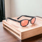 The original KD's 2128 sunglasses with orange polycarbonate lenses and a durable black frame placed on a wooden furniture.