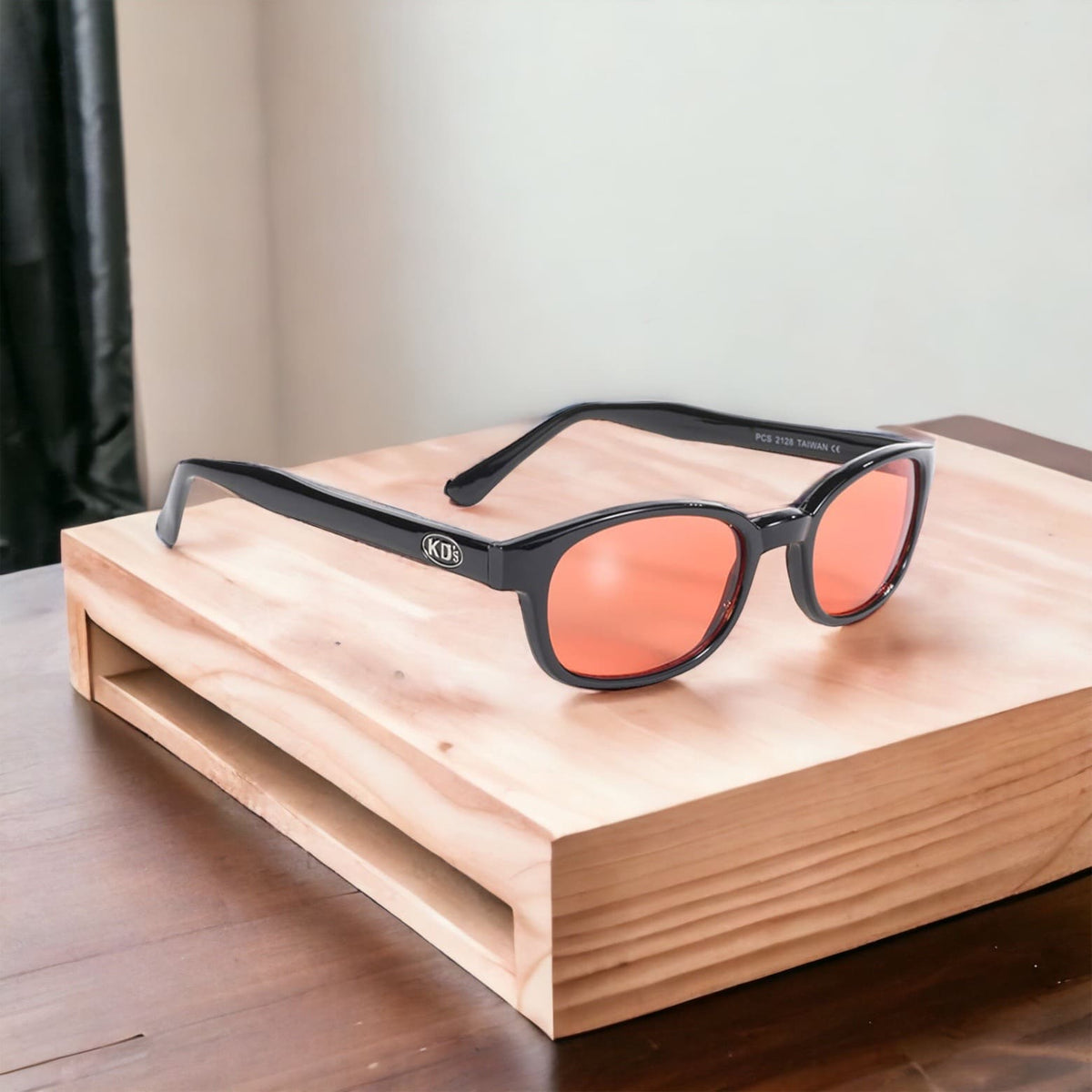 The original KD's 2128 sunglasses with orange polycarbonate lenses and a durable black frame placed on a wooden furniture.