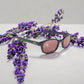 KD's 22120 sunglasses that fit under a motorcycle or ski helmet. For bikers and sportsmen. With a stylish black frame and pink lenses. Set on a white surface surrounded by lavender.