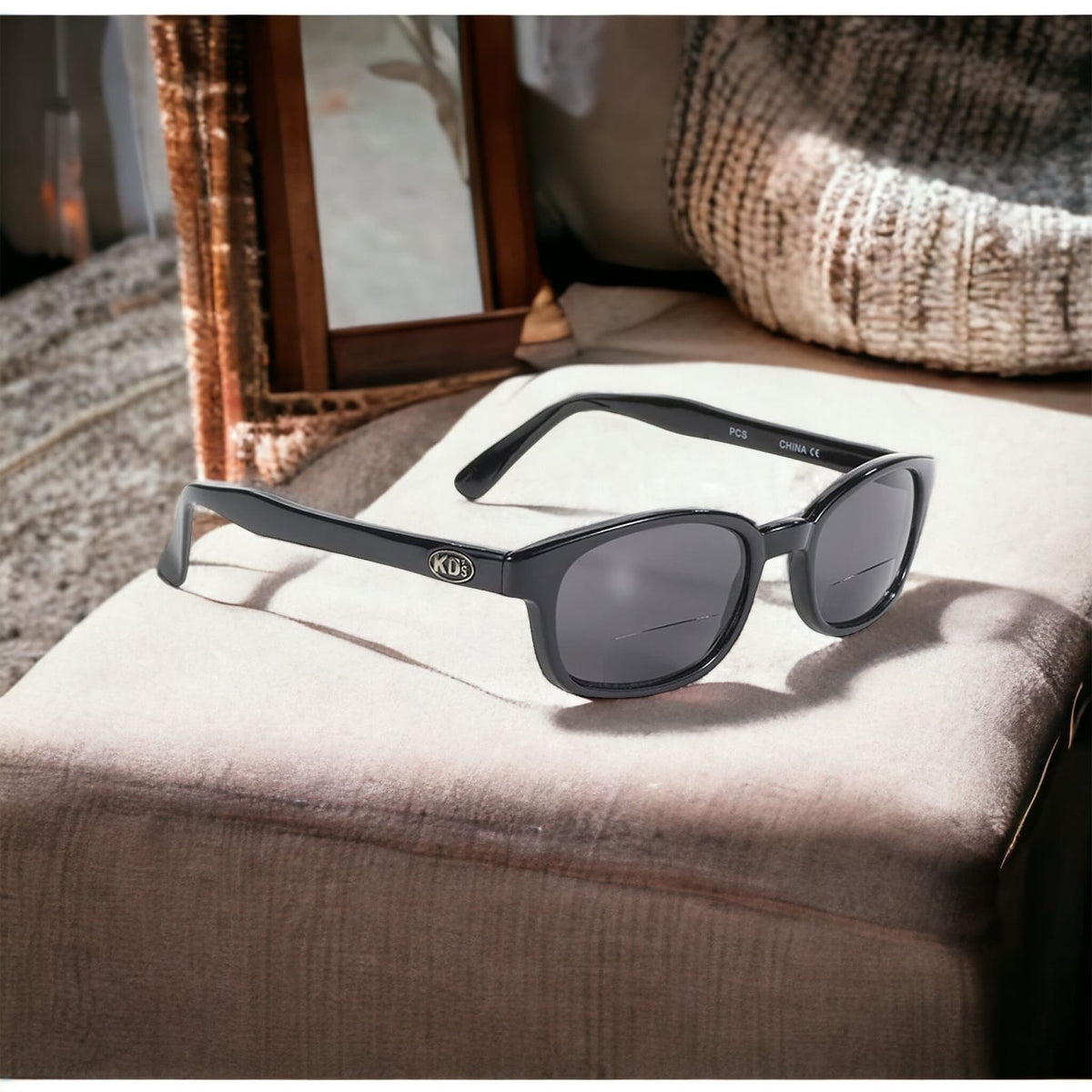 KD's readerz sunglasses with correction index. Worn by Jax Teller in Sons of Anarchy. With elegant black frames and dark grey lenses. Sitting on a comfortable couch.