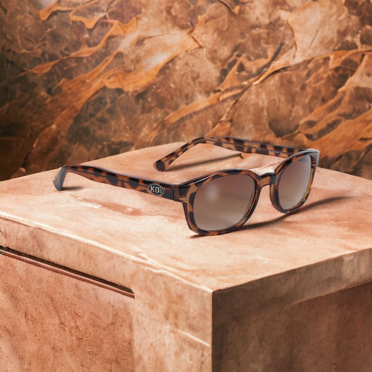 X-KD's 100 sunglasses with amber lenses and a frame with turtle shell motifs placed on a marble countertop