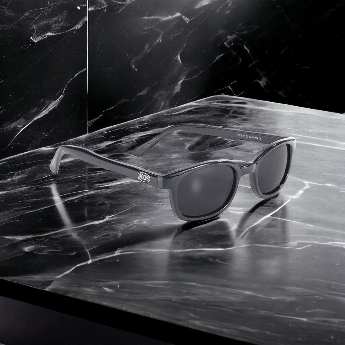 X-KD's 1120 sunglasses with dark grey lenses and a refined black frame placed on a black marble countertop.